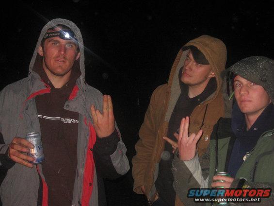 Three guys in hoodies and jackets holding cans, one wearing a headlamp