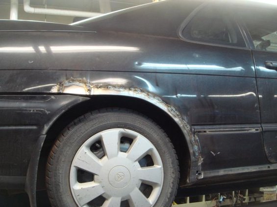 Black car rear fender with visible welding repairs around the wheel well