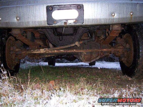 Underside view of a truck's rear axle, leaf springs, and differential. License plate area visible above