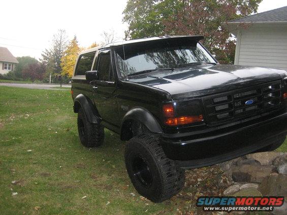 Black Ford Bronco parked on grass with a house and trees in background
