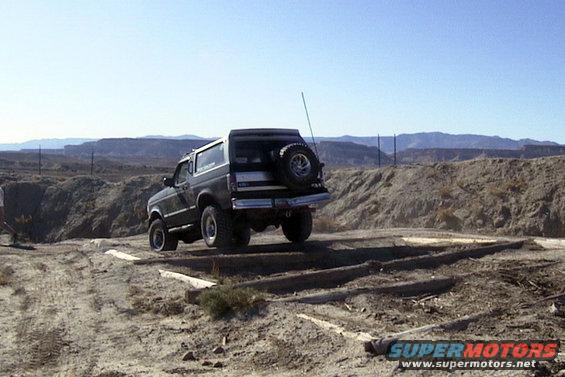 Dark green 1994 Ford Bronco driving over wooden obstacles in a desert landscape