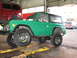 1975 Ford Bronco - A green Ford Bronco is raised on a hydraulic lift inside a garage, with other vehicles visible.