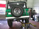 1975 Ford Bronco - Rear view of a green 1975 Ford Bronco on a lift in a garage, showing the spare tire and exhaust.