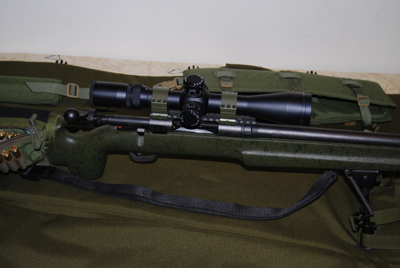 Green speckled rifle with scope and bipod, ammo visible on the side