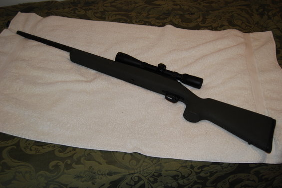 Black rifle with scope, lying on a white towel over a patterned blanket