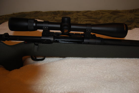 Rifle with a black scope mounted on top. The rifle has a dark green stock