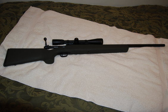 Rifle with a scope mounted on top, resting on a white blanket