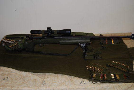 Green rifle with scope and bipod, resting on a green mat with ammunition clips