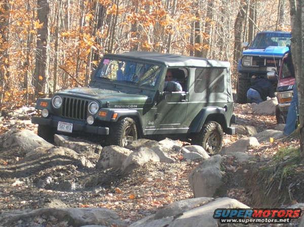 Green Jeep Wrangler Rubicon navigating rocky terrain with other vehicles in background