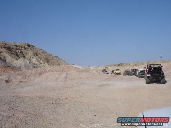 Several off-road vehicles driving in a desert with rocky hills