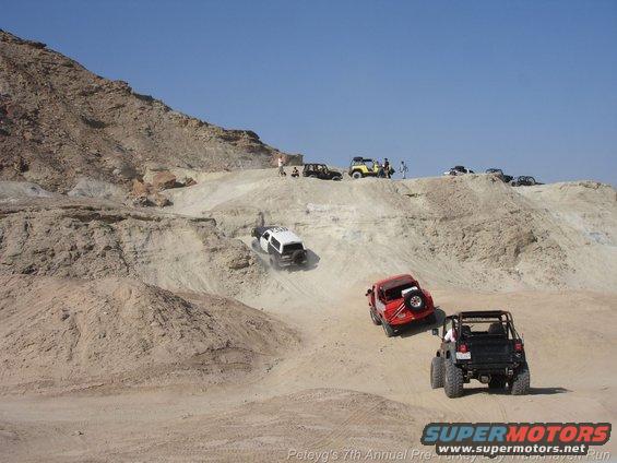 Several off-road vehicles navigate a steep, sandy terrain under a clear blue sky