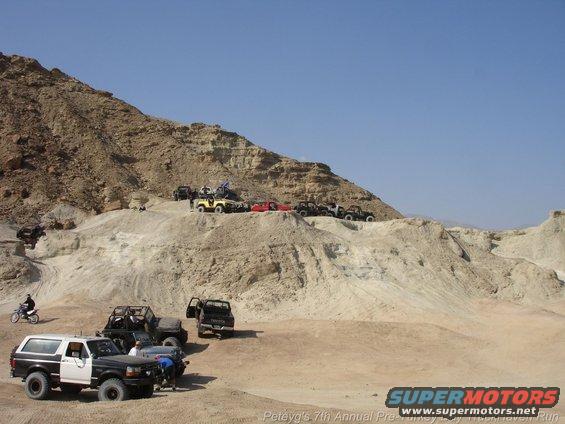 Two-tone 1994 Ford Bronco parked on dirt, 3q-front view. Other off-road vehicles in background