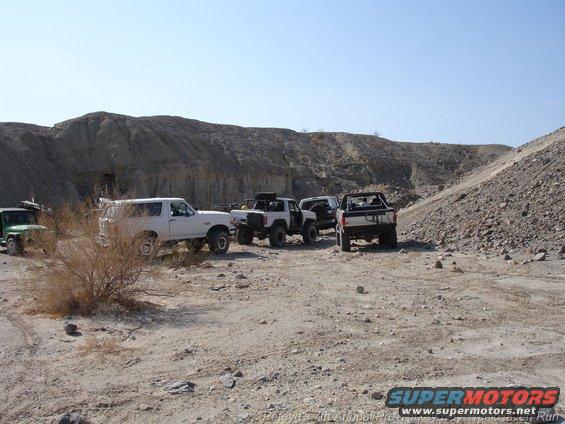 Several off-road vehicles parked in a desert canyon, including a white 1994 Ford Bronco