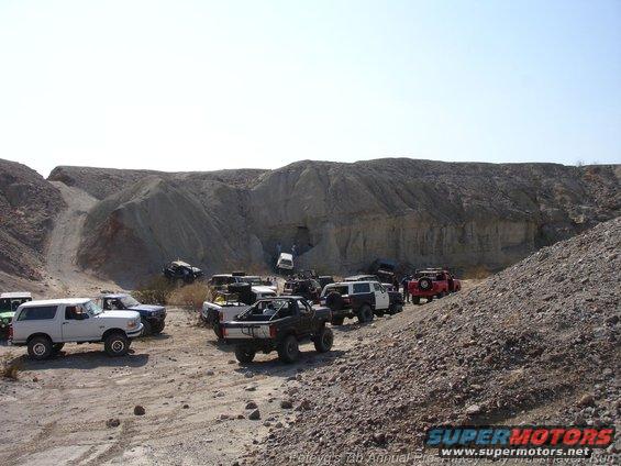 Group of off-road vehicles gathered in a rocky quarry, some parked, some on inclines