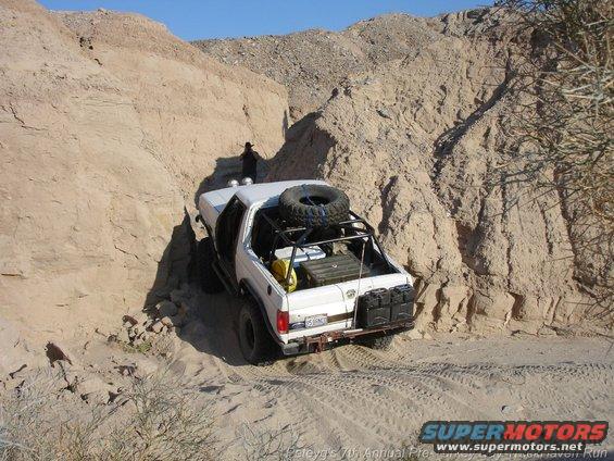 White 1994 Ford Bronco with spare tire on roof rack navigating a sandy canyon