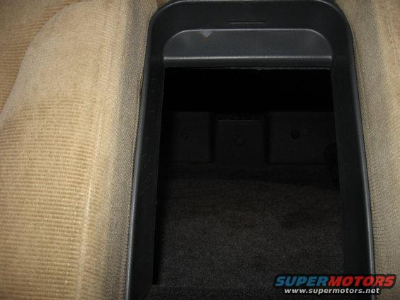 Car interior shot of an open center console storage bin with tan fabric seats visible to the left
