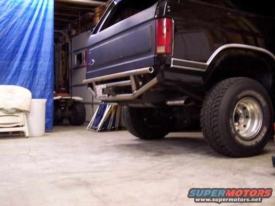 Rear view of a dark-colored Ford Bronco with an aftermarket bumper. An ATV is visible to the left