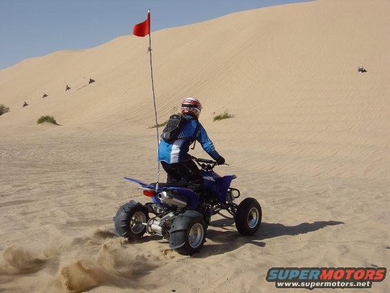 Blue ATV with a rider kicking up sand, red flag on pole