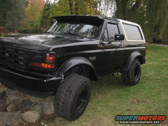 Black 1995 Ford Bronco with large tires and white top parked on rocks and grass