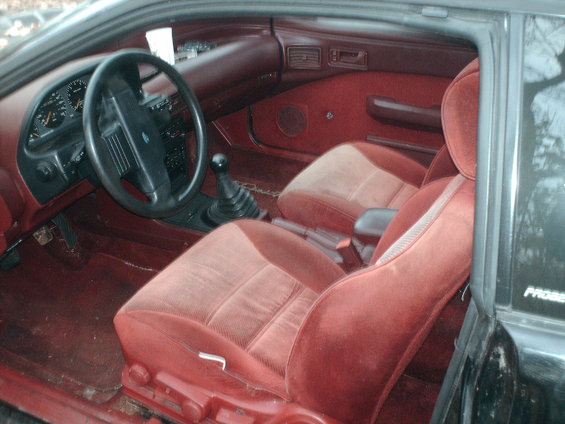 Red velour interior of a 1993 Ford Probe, showing the dashboard, steering wheel, gear shifter, and front seats