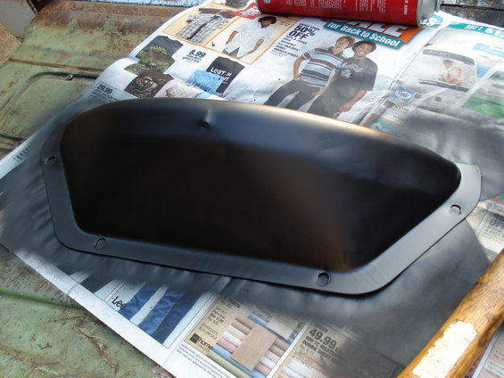 Black painted automotive part with mounting holes, resting on newspaper