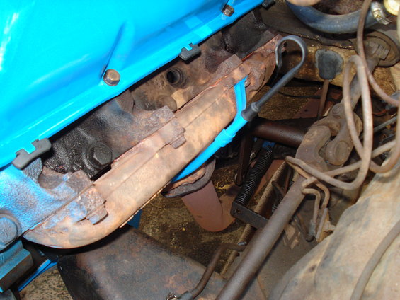 Close-up of a rusty exhaust manifold with a blue spark plug wire holder attached