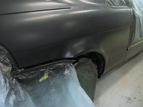 Close-up of a car's rear fender and door, covered in plastic sheeting for painting