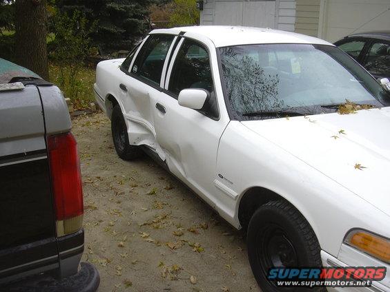 White sedan with severe side damage, parked next to a dark pickup truck
