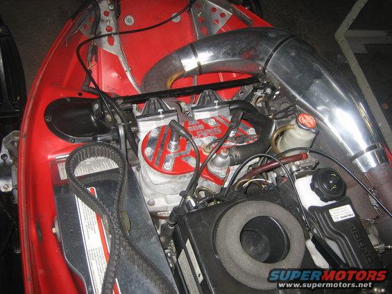 Red snowmobile engine with chrome exhaust pipe and visible belt