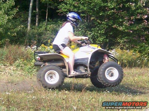 Yellow and white all-terrain vehicle with a rider in a blue helmet, mid-air over a grassy field