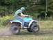 1994 Polaris TRAIL BOSS 325 - A rider on a teal and white all-terrain vehicle jumps over a dirt patch.