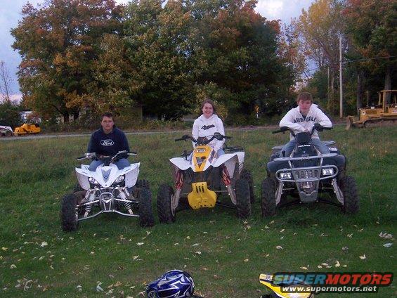 Three ATVs with riders in front view, one white, one white and yellow, one black