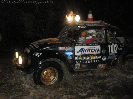 Black Volkswagen Beetle Baja race car with number 1102, driving through water at night