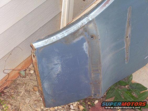 Blue car fender section with rust on the edge and mounting holes