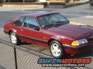 Red 1988 Ford Mustang coupe parked next to a chain-link fence