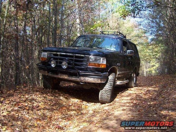 Black 1996 Ford Bronco with bull bar and off-road tires on a wooded trail