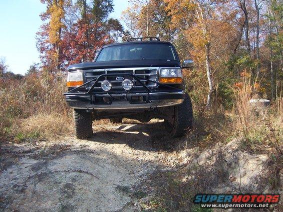 Black Ford Bronco on dirt road, front view. Bull bar with lights attached
