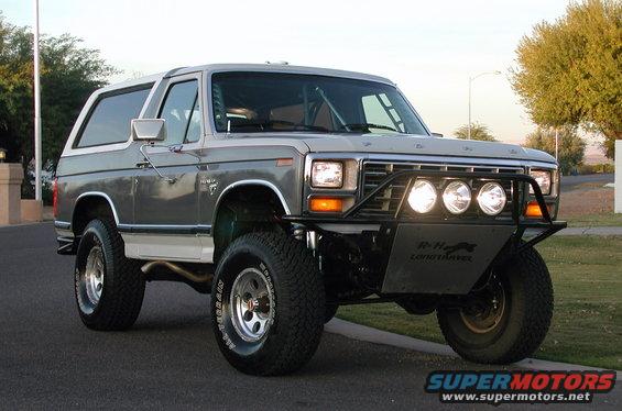 Gray and white 1978 Ford Bronco with off-road lights and bumper, parked on a street