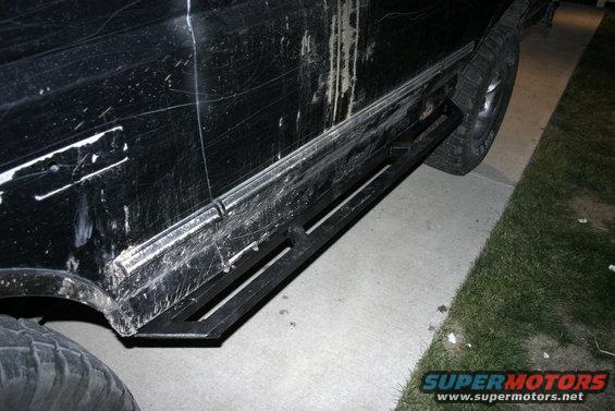 Black SUV side panel with heavy scratches and aftermarket sliders installed