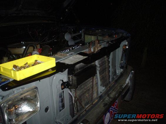 Vehicle front end with hood open, showing engine bay, radiator, and a yellow parts tray