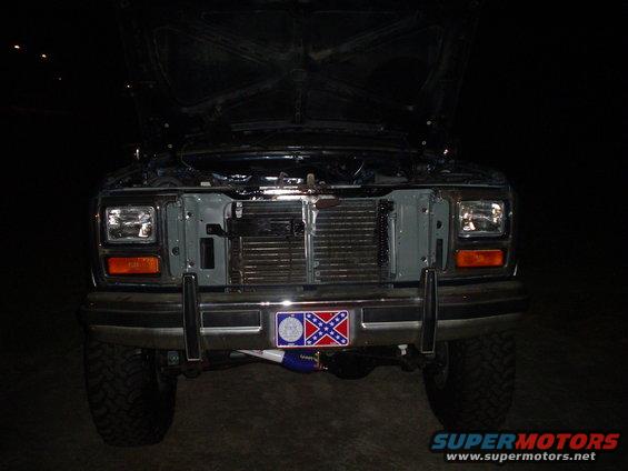 Front of a Ford truck with hood open. Has a confederate flag license plate frame