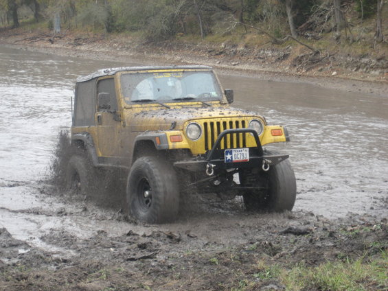 Yellow 2001 Jeep Wrangler splashing through mud