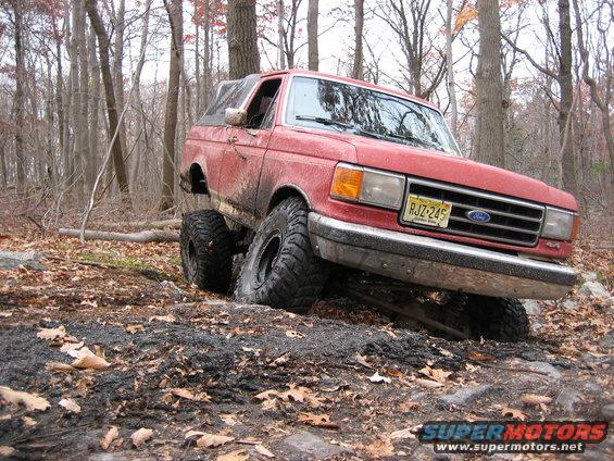 Red Ford Bronco with lifted suspension stuck on rocky terrain, front 3/4 view