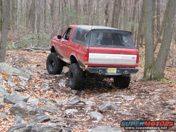Red 1990 Ford Bronco with soft top on rocky trail