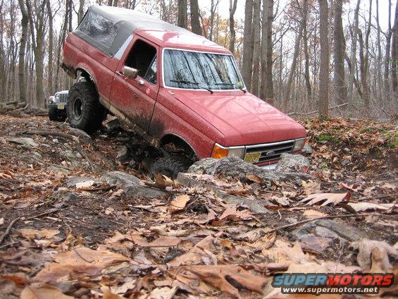 Red 1990 Ford Bronco navigating rocky terrain with a Jeep in the background