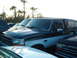 1995 Ford F-150 - A dark green and white pickup truck with a camper shell is parked in a lot with other vehicles and palm trees.
