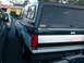 1995 Ford F-150 - A dark green and silver Ford Bronco with a camper shell is parked next to another vehicle.