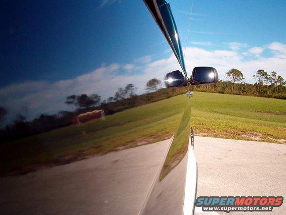 Reflection of a grassy hill and trees in the side of a dark-colored vehicle. A side mirror is visible