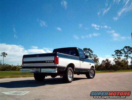 Rear view of a two-tone Ford F-Series truck parked on asphalt under a blue sky