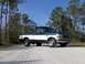 1995 Ford F-150 - A two-tone 1995 Ford F-150 pickup truck is seen from a three-quarter front view on a dirt road with trees in the background.